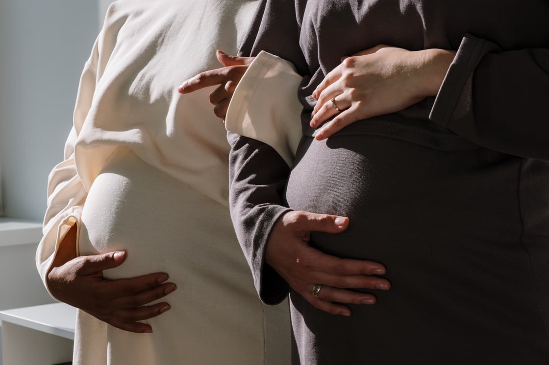 Two pregnant women locking arms and holding bellies